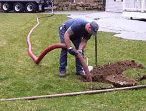Septic pumping technician servicing a residential septic tank with a vacuum hose in Norton, MA