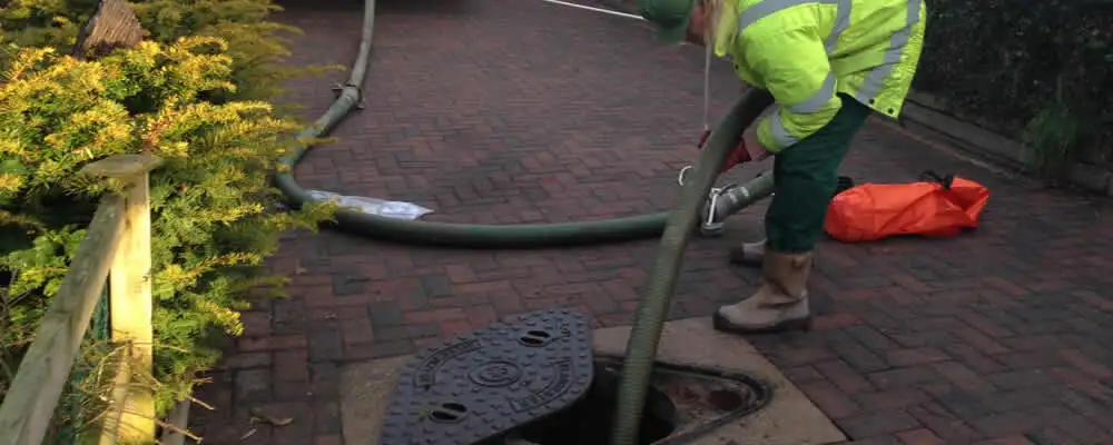 Septic tank cleaning technician servicing a septic tank with a vacuum hose in Norton, MA