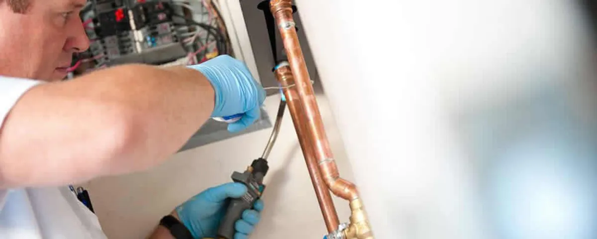Water heater repair technician testing copper pipe connections and controls in Norton, MA