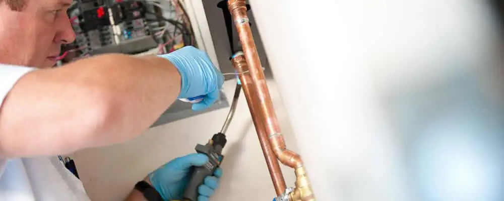 Water heater repair technician testing copper pipe connections and controls in Norton, MA